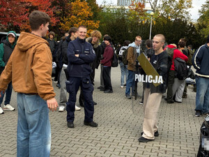 Zdjęcie przedstawia policjanta stojącego przy młodym chłopaku trzymającym  policyjną tarczę w rękach.